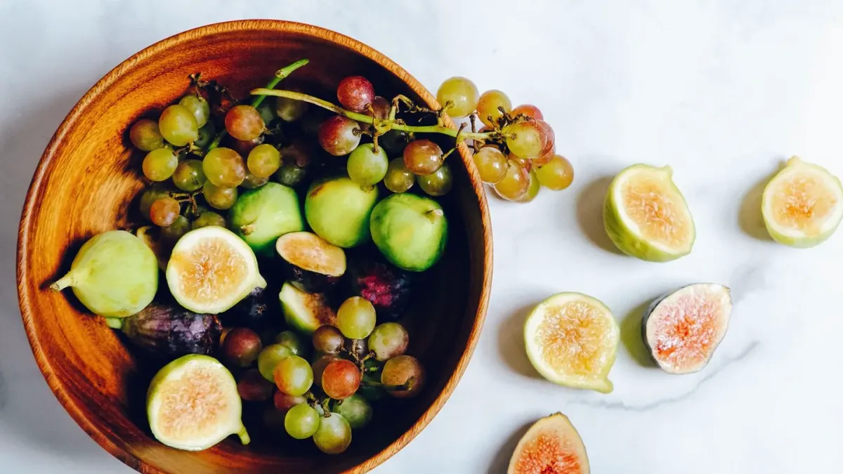 A bowl of grapes sitting on a kitchen counter while a dog watches from a few feet away
