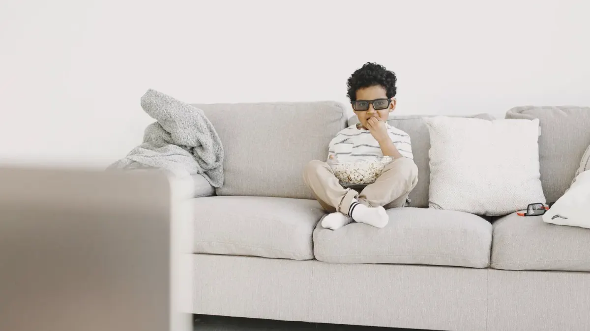 A dog sitting attentively near a bowl of popcorn on a couch