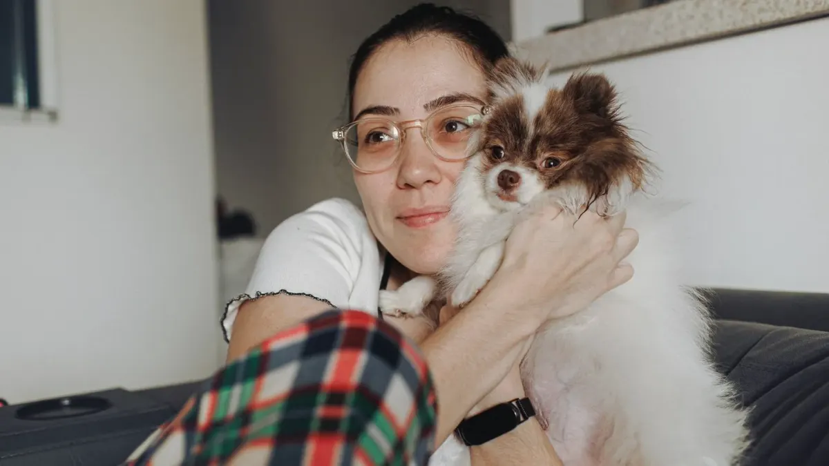 A dog waiting beside its bowl while an owner reads a pet food label in the kitchen