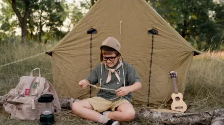A dog wearing a trail harness resting outside a tent at a forest campsite