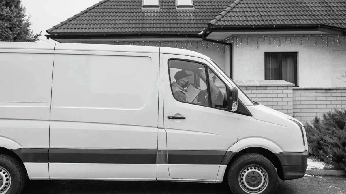 A mobile grooming van parked in a driveway with a groomer greeting a leashed dog