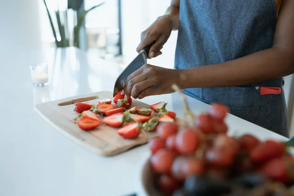 A person slicing fresh strawberries on a cutting board while a dog waits nearby