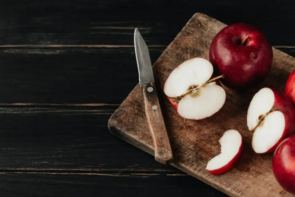 Cored apple slices on a cutting board beside a whole apple with visible seeds
