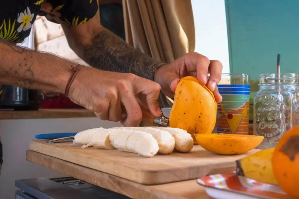Hands slicing a peeled banana into thin rounds on a cutting board