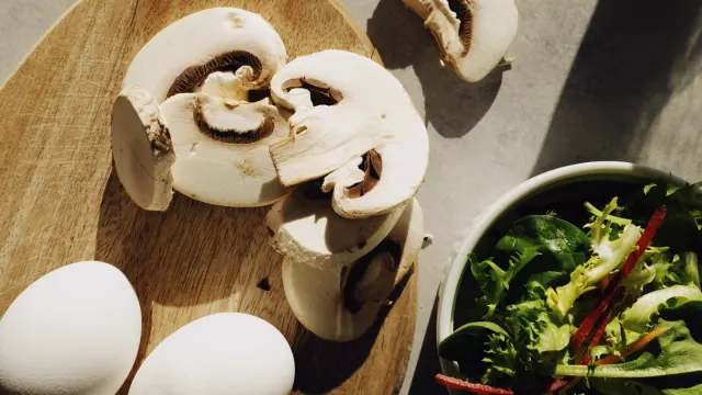 Sliced white button mushrooms on a wooden cutting board with a dog looking on