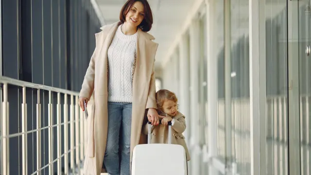 Traveler carrying a small dog in a soft-sided carrier through an airport terminal